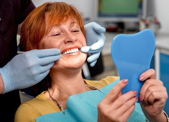 An older woman admiring her new dentures in a hand mirror