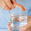 Someone placing dentures in a glass of solution