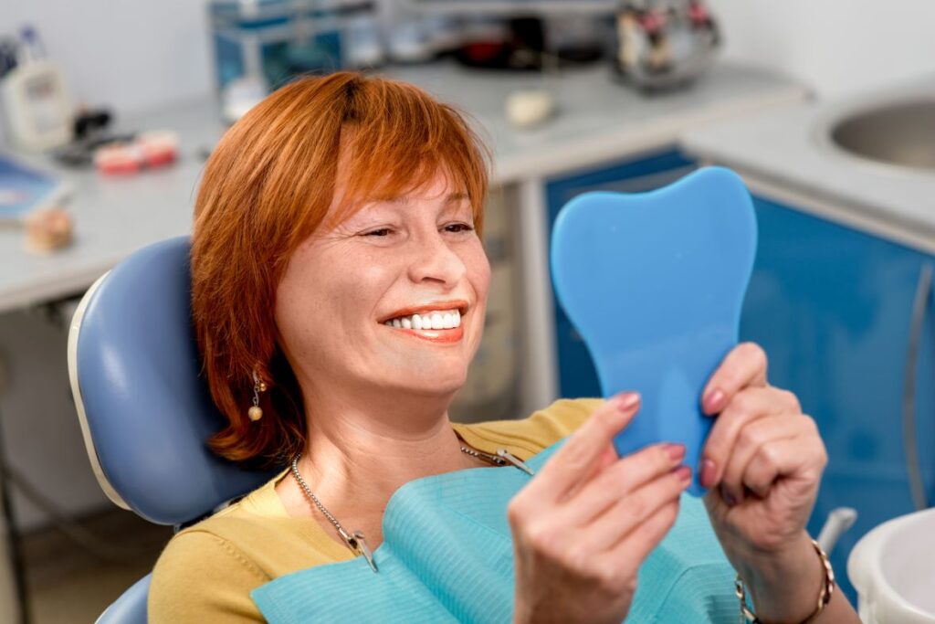 A woman looking in the mirror at her smile in a dental office.